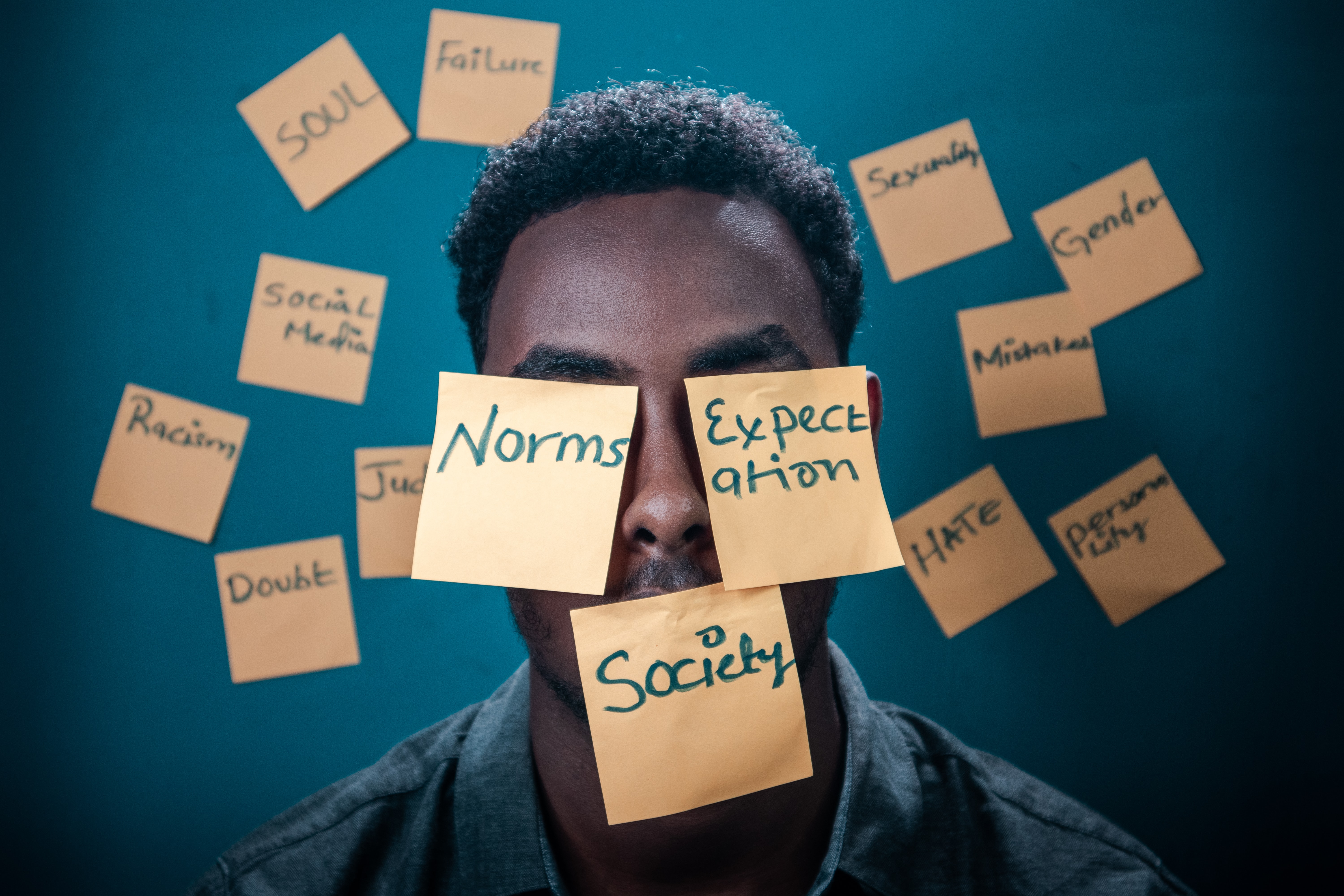 Black man against dark blue background with words written on post-its on his face